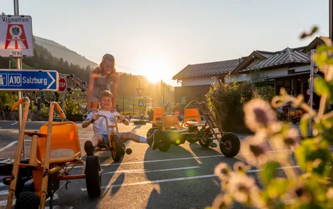 "Good Life" Familien-Vorteilswochen Kinder spielen mit Tretkarts an einem sonnigen Tag im Freien bei Salzburg